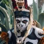 native mexican aztec warrior with pre hispanic makeup simulating a skull and a bone headdress adorned with feathers and cempazuchil flowers