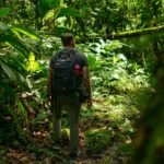 man carrying black backpack standing beside trees