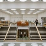 black man with book near stairs in public library