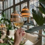 crop woman with glass of wine in room with green plants